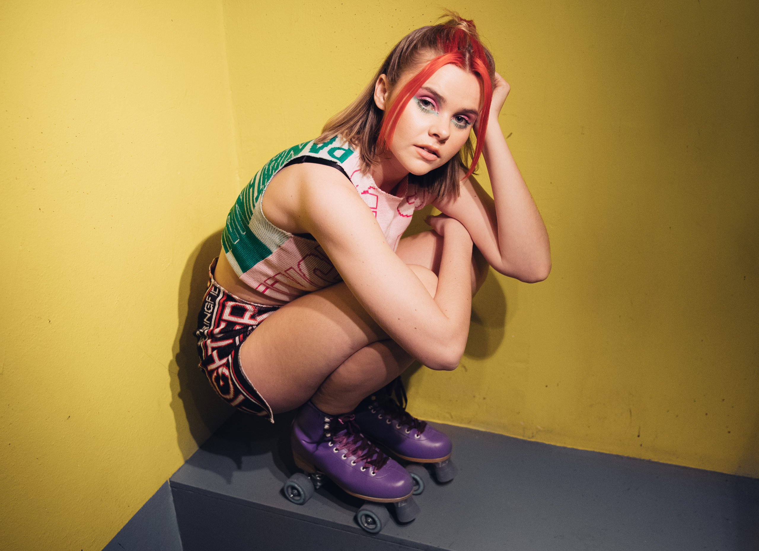 Hedda Mae sitter på huk med ryggen til en gul vegg. Foto: Alvin Santos